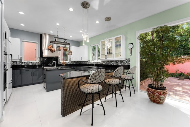 kitchen with a center island, a kitchen bar, a healthy amount of sunlight, white cabinets, and wall chimney exhaust hood