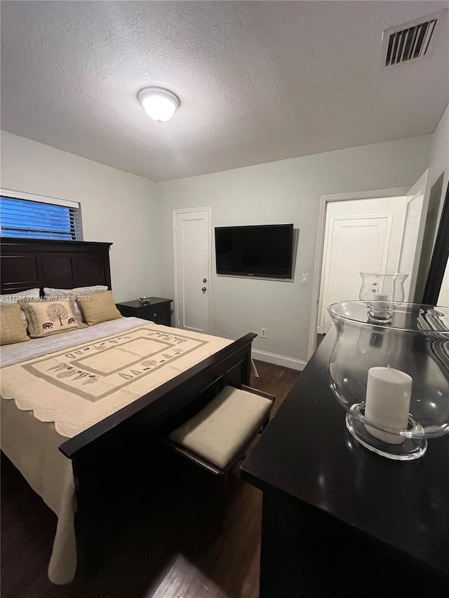 bedroom with dark wood-type flooring, baseboards, visible vents, and a textured ceiling