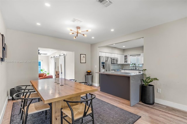 dining area featuring ceiling fan with notable chandelier, sink, and light wood-type flooring