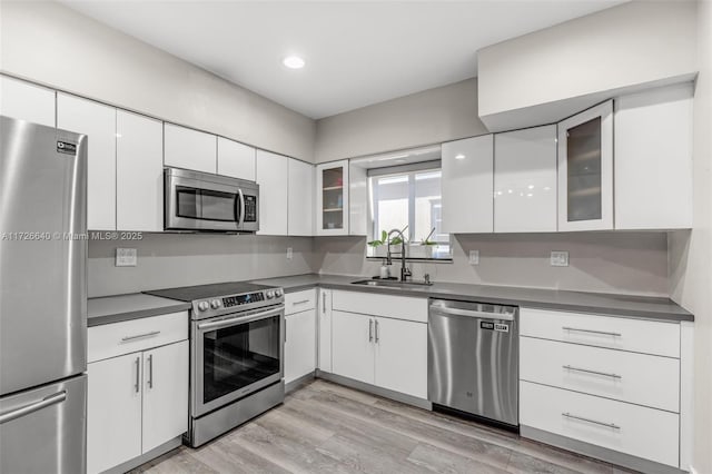 kitchen with sink, light wood-type flooring, white cabinetry, and appliances with stainless steel finishes