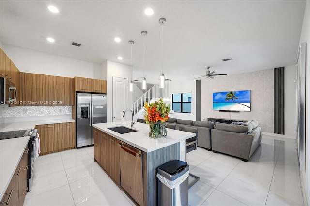 kitchen featuring a kitchen island with sink, appliances with stainless steel finishes, hanging light fixtures, ceiling fan, and sink