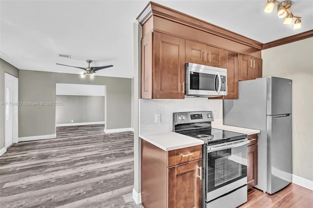 kitchen featuring appliances with stainless steel finishes, light wood-type flooring, crown molding, ceiling fan, and decorative backsplash