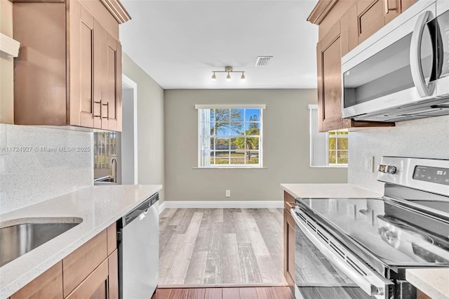 kitchen featuring sink, light stone counters, light wood-type flooring, backsplash, and appliances with stainless steel finishes