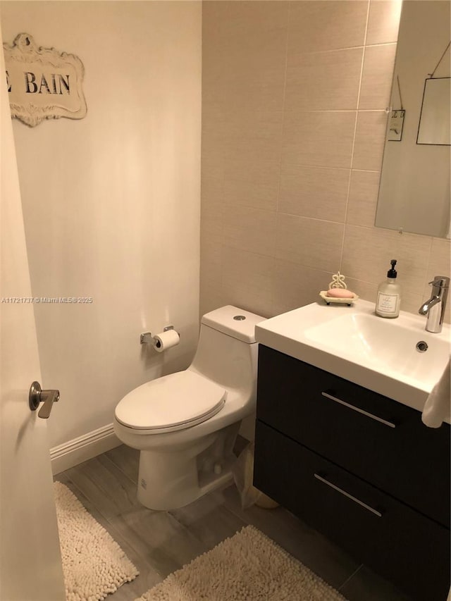 bathroom featuring toilet, decorative backsplash, vanity, and tile walls