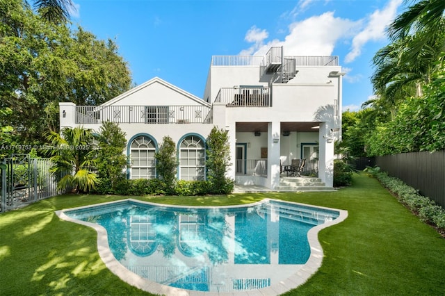 back of house with a balcony, a fenced in pool, a patio area, and a lawn