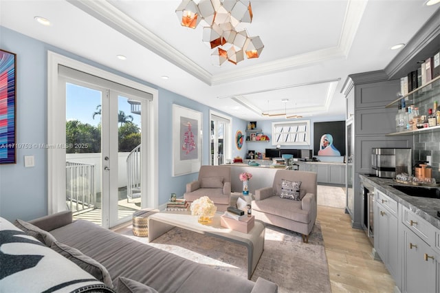 living room featuring sink, french doors, light hardwood / wood-style floors, a tray ceiling, and crown molding