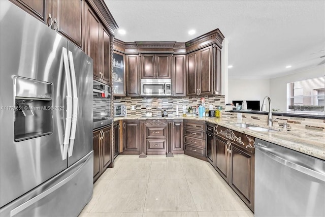 kitchen with stainless steel appliances, light stone countertops, sink, dark brown cabinets, and tasteful backsplash