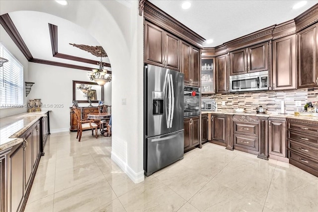 kitchen with stainless steel appliances, crown molding, light stone countertops, dark brown cabinets, and backsplash