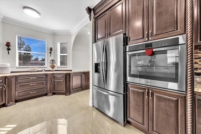 kitchen with a textured ceiling, stainless steel appliances, dark brown cabinets, and crown molding