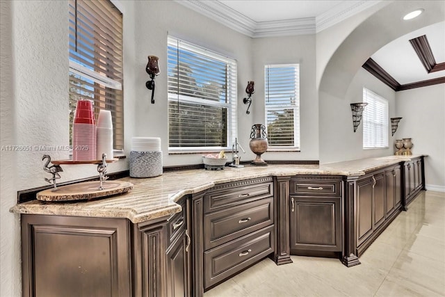 kitchen featuring light stone countertops, ornamental molding, and dark brown cabinets