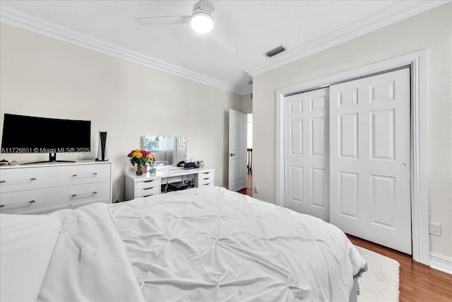 bedroom with hardwood / wood-style flooring, ceiling fan, a closet, and crown molding