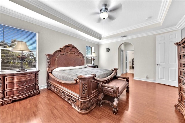 bedroom with hardwood / wood-style floors, a raised ceiling, ceiling fan, and ornamental molding