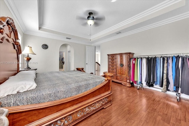 bedroom with wood-type flooring, a raised ceiling, ceiling fan, and crown molding