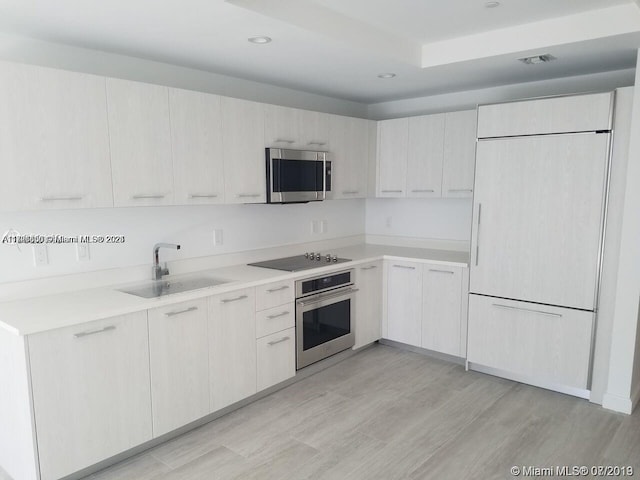 kitchen with sink, white cabinets, light wood-type flooring, and appliances with stainless steel finishes