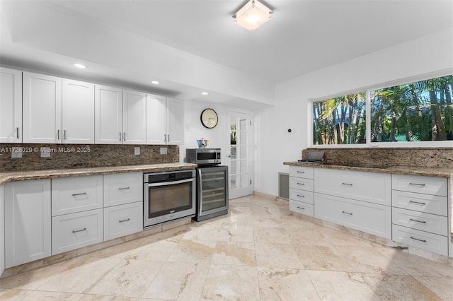 kitchen with stainless steel appliances, decorative backsplash, beverage cooler, white cabinets, and dark stone countertops