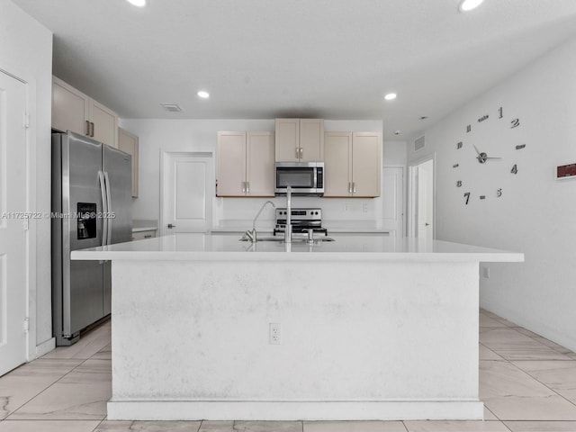 kitchen featuring appliances with stainless steel finishes, sink, a kitchen island with sink, and cream cabinetry