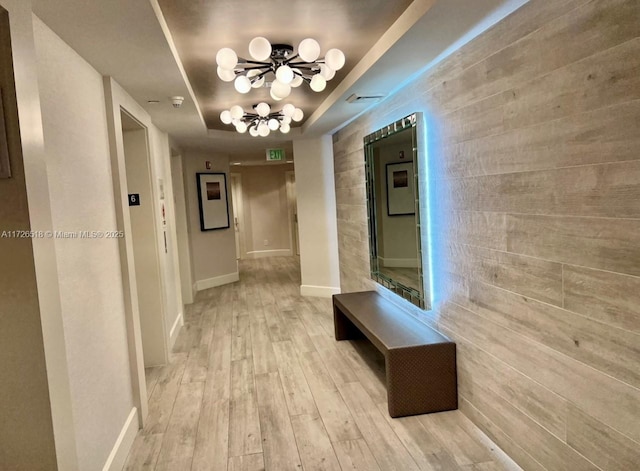 hallway featuring an inviting chandelier, a tray ceiling, and light hardwood / wood-style flooring