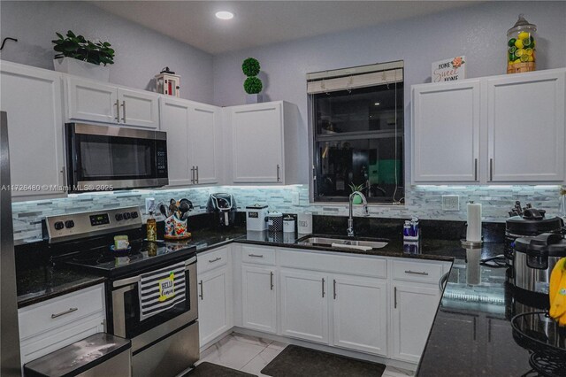 kitchen with sink, dark stone countertops, stainless steel appliances, decorative backsplash, and white cabinets