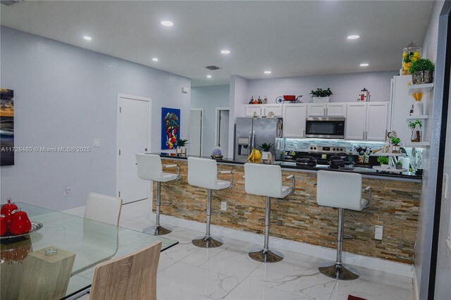 kitchen featuring white cabinetry, backsplash, stainless steel appliances, and a kitchen breakfast bar