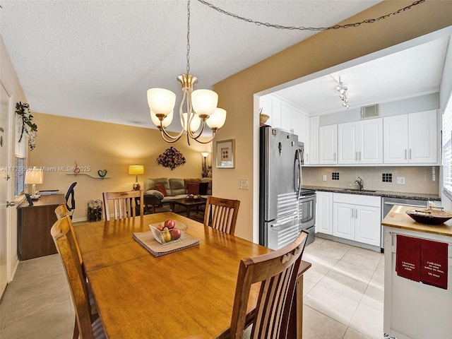 dining space with sink, light tile patterned flooring, a textured ceiling, and a notable chandelier