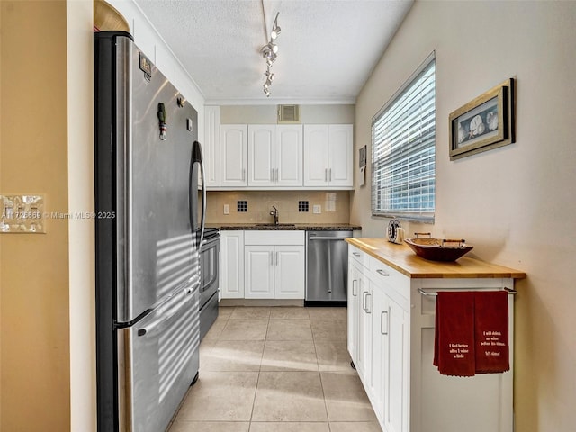 kitchen featuring stainless steel appliances, light tile patterned flooring, white cabinetry, and a textured ceiling