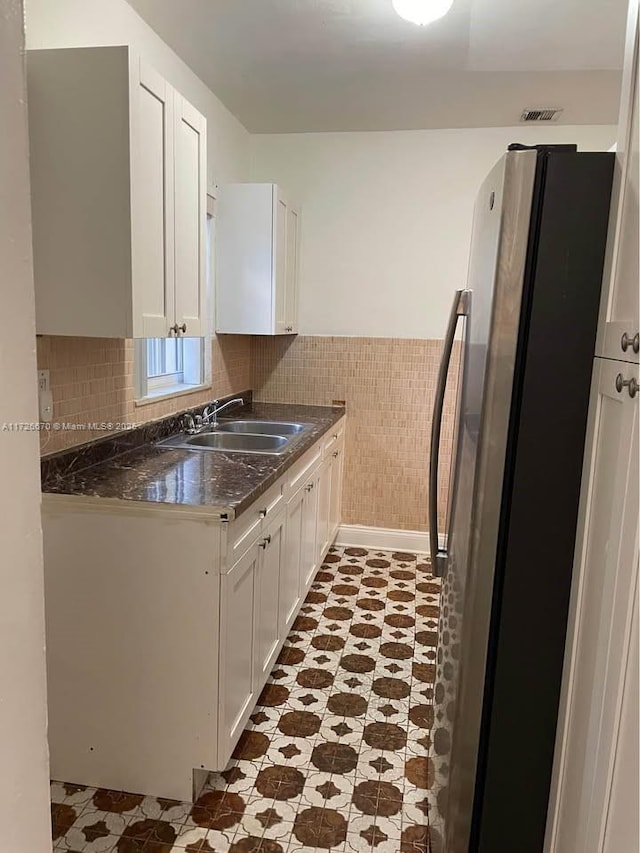 kitchen with sink, tile walls, white cabinets, and stainless steel refrigerator