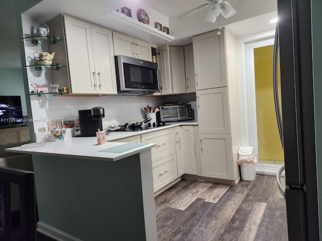 kitchen with a peninsula, a toaster, wood finished floors, light countertops, and black appliances