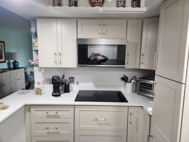 kitchen featuring black electric cooktop, light countertops, a toaster, and stainless steel microwave