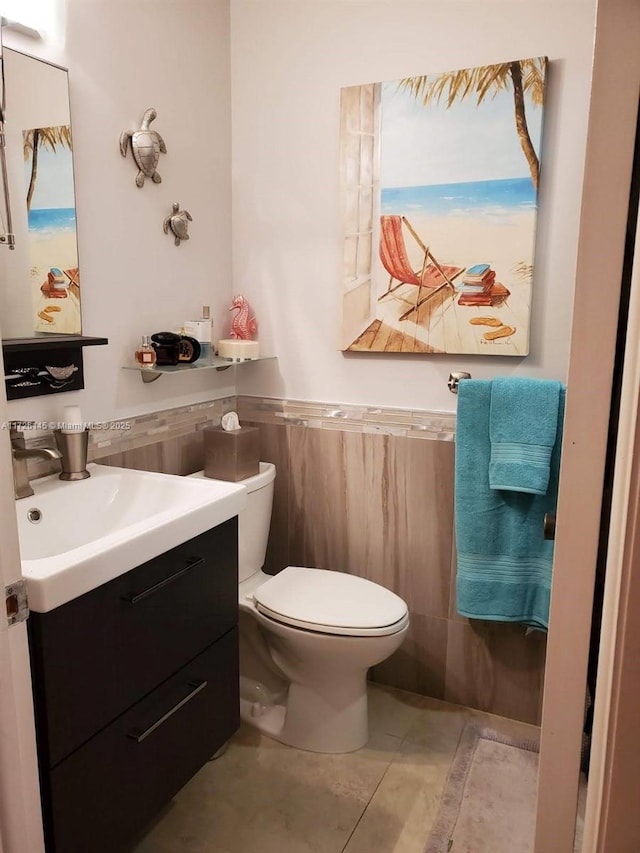 bathroom with wainscoting, toilet, vanity, and tile walls