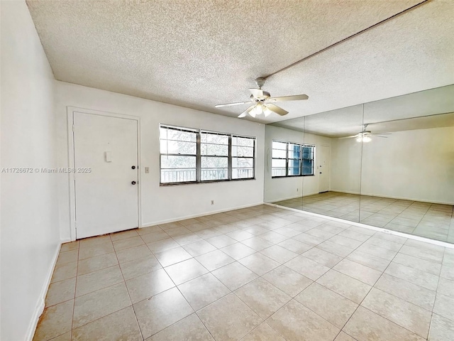 empty room featuring ceiling fan, light tile patterned flooring, and a textured ceiling