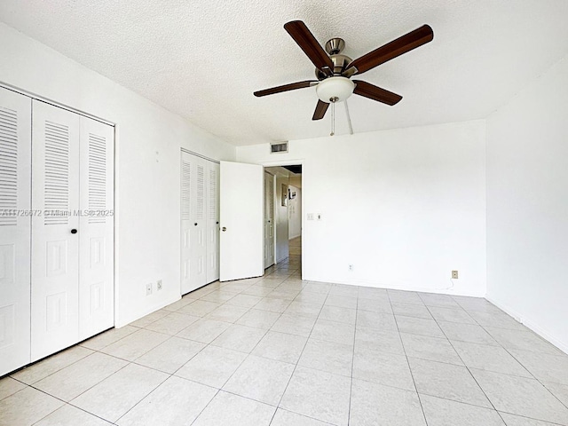 unfurnished bedroom with multiple closets, ceiling fan, light tile patterned flooring, and a textured ceiling