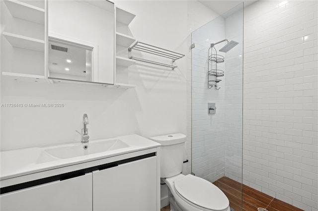 bathroom with toilet, tiled shower, and vanity