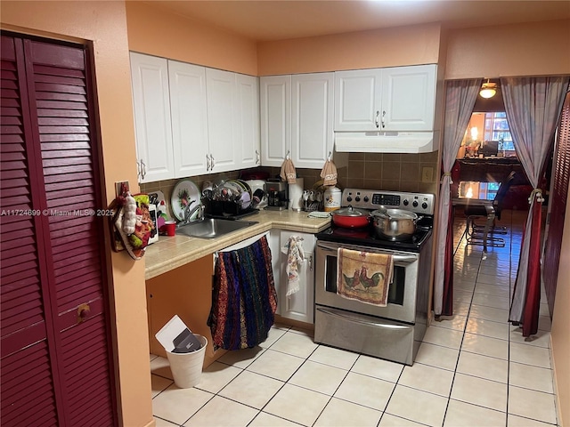 kitchen featuring stainless steel range with electric stovetop, white cabinetry, backsplash, light tile patterned flooring, and sink