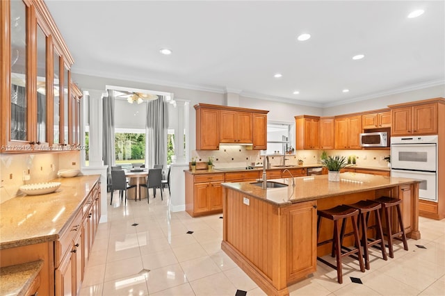 kitchen featuring white double oven, a kitchen island with sink, ceiling fan, ornamental molding, and sink