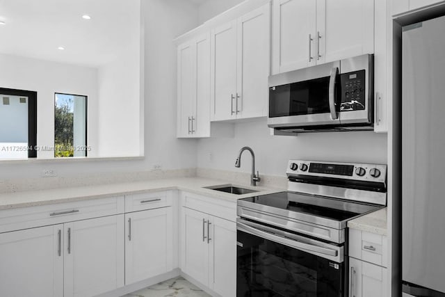 kitchen with white cabinetry, sink, light stone counters, and appliances with stainless steel finishes