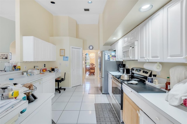 kitchen with stainless steel electric stove, a high ceiling, light tile patterned flooring, and white cabinetry