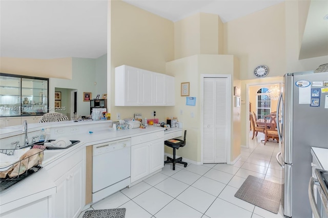 kitchen featuring stainless steel refrigerator, light tile patterned floors, high vaulted ceiling, white cabinetry, and white dishwasher