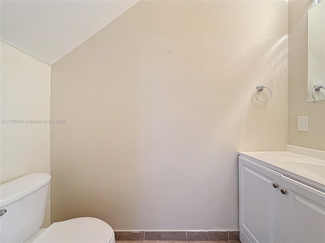 bathroom featuring toilet, vaulted ceiling, and vanity