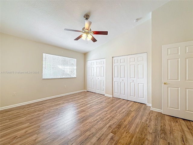 unfurnished bedroom with a textured ceiling, lofted ceiling, multiple closets, ceiling fan, and hardwood / wood-style flooring