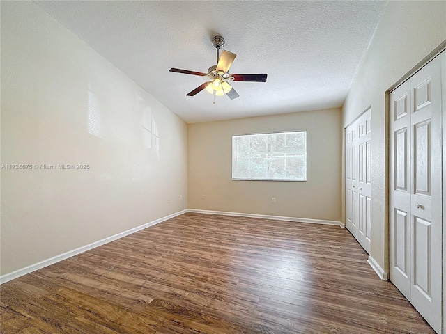 unfurnished bedroom with ceiling fan, dark wood-type flooring, two closets, and a textured ceiling