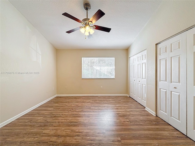 unfurnished bedroom featuring wood-type flooring, two closets, ceiling fan, and a textured ceiling