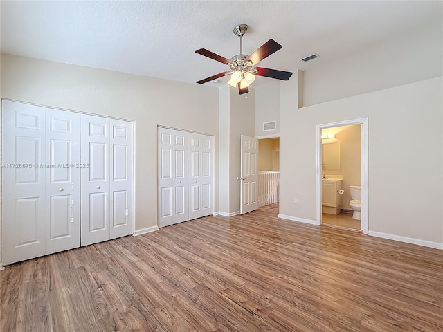 unfurnished bedroom with hardwood / wood-style floors, connected bathroom, ceiling fan, high vaulted ceiling, and two closets