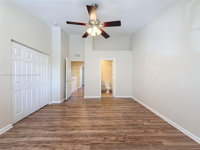 unfurnished bedroom with connected bathroom, a closet, a towering ceiling, ceiling fan, and dark hardwood / wood-style floors