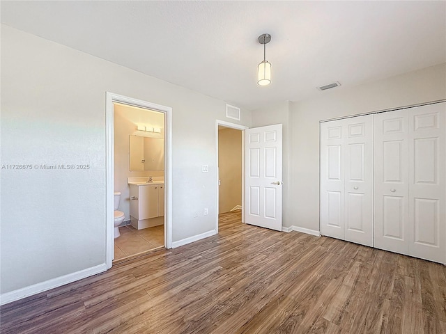 unfurnished bedroom featuring sink, ensuite bathroom, a closet, and hardwood / wood-style floors