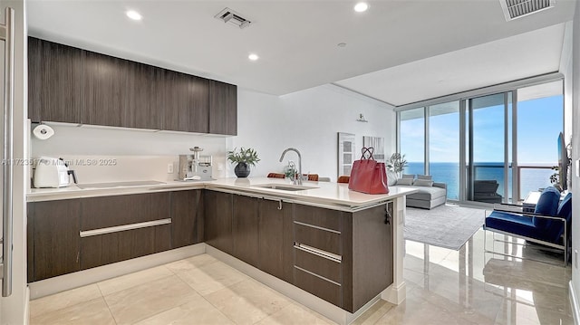 kitchen featuring sink, a water view, kitchen peninsula, dark brown cabinetry, and floor to ceiling windows