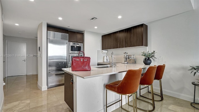 kitchen with sink, stainless steel built in fridge, a kitchen bar, kitchen peninsula, and dark brown cabinetry