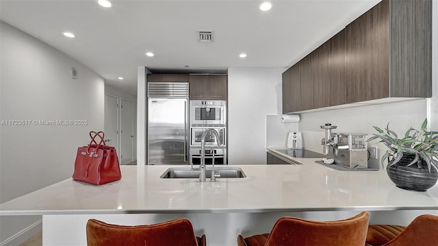 kitchen with a breakfast bar area, stainless steel appliances, kitchen peninsula, dark brown cabinetry, and sink