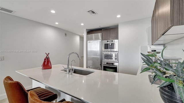 kitchen with stainless steel built in refrigerator, sink, dark brown cabinets, and kitchen peninsula