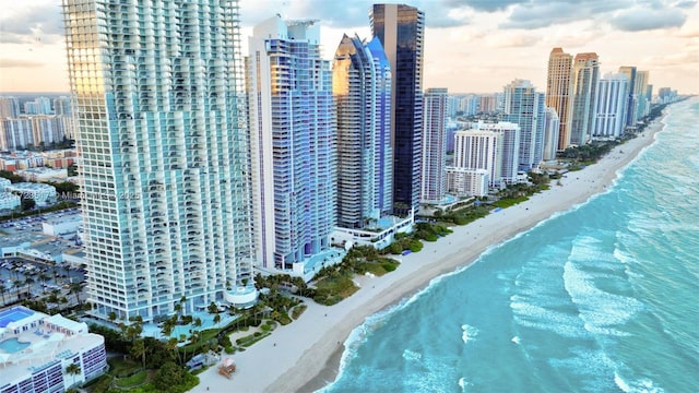 aerial view at dusk featuring a view of the beach and a water view