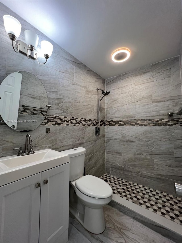 bathroom featuring toilet, vanity, tile walls, and tiled shower